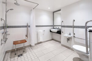 A modern bathroom with a shower, toilet, sink, and a wooden bench.