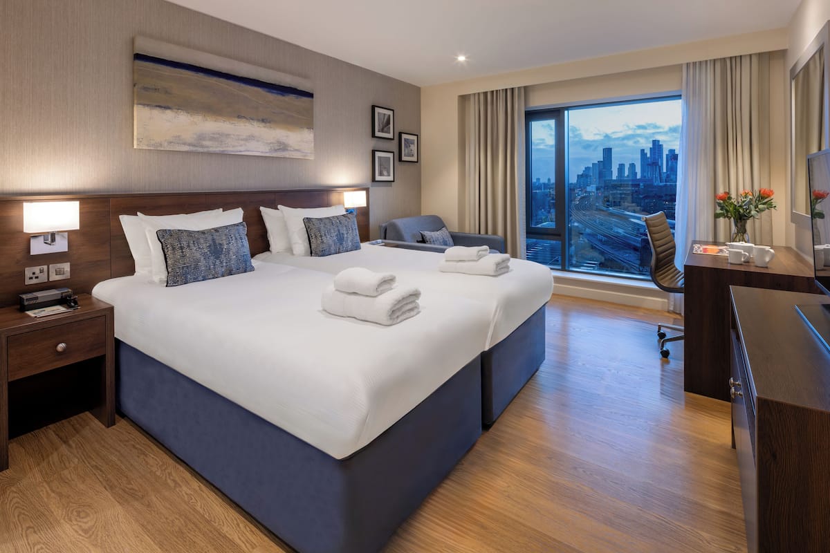 Une chambre d’hôtel moderne, dotée d’un grand lit, d’un bureau et offrant une vue sur le paysage urbain.