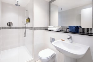 A modern bathroom with a glass-enclosed shower, a white toilet, and a sink with a mirror above.