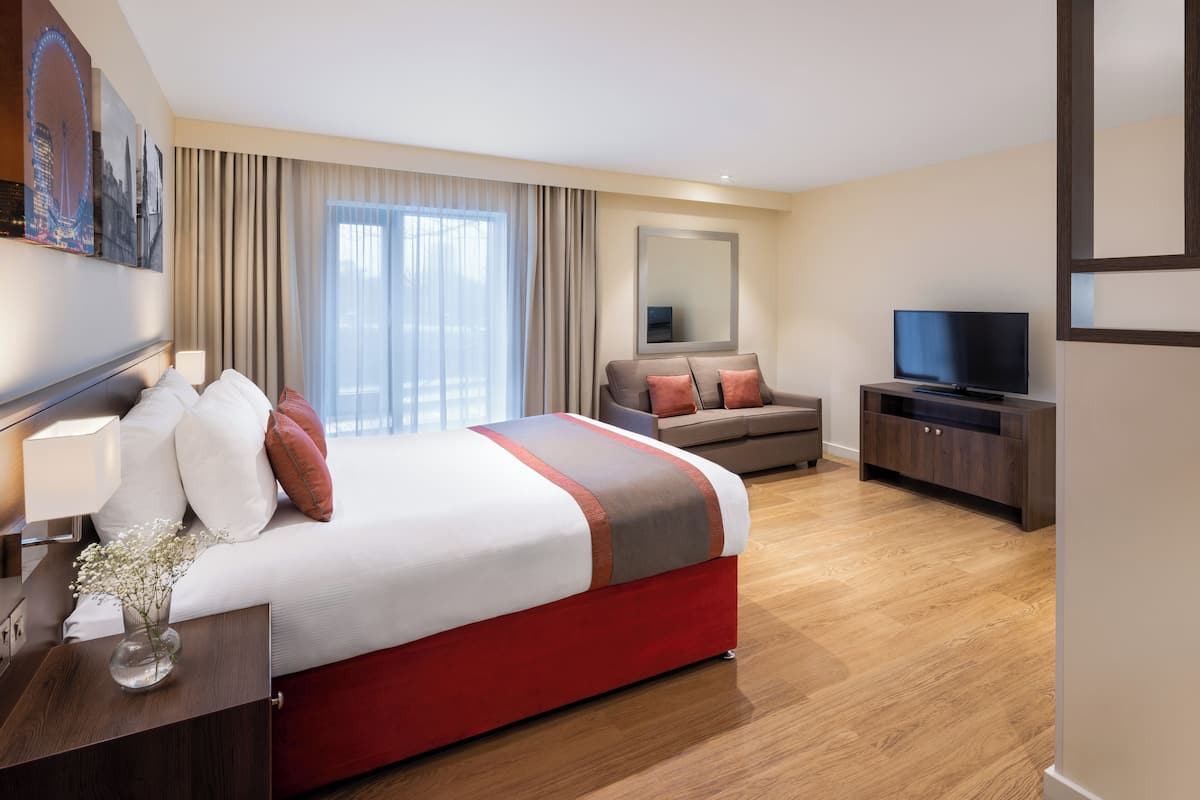 Une chambre d’hôtel avec un grand lit, un canapé, une télévision et une fenêtre avec des rideaux.