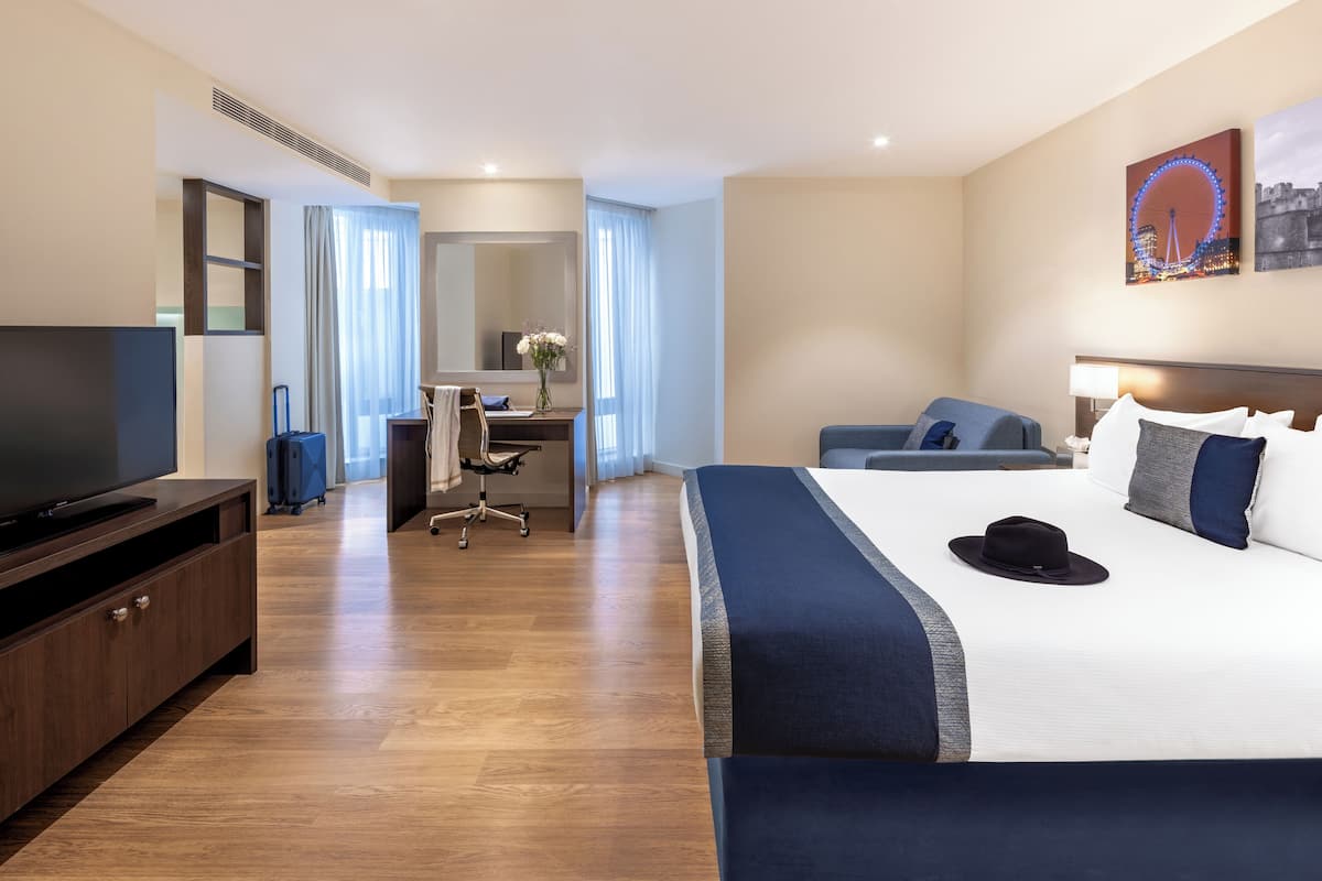 Une chambre d’hôtel avec un grand lit, un bureau avec une chaise, une télévision et une grande fenêtre avec des rideaux.