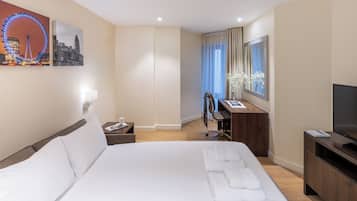 A hotel room with a large bed, a desk with a chair, a TV, and artwork on the walls.