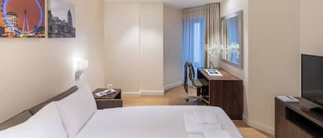 A hotel room with a large bed, a desk with a chair, a TV, and artwork on the walls.