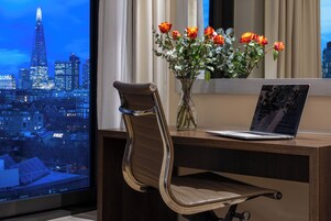 A desk with a laptop, a vase with flowers, and a chair.