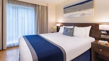 Una habitación de hotel con una cama grande, una mesita de noche, una lámpara y un cuadro en la pared.