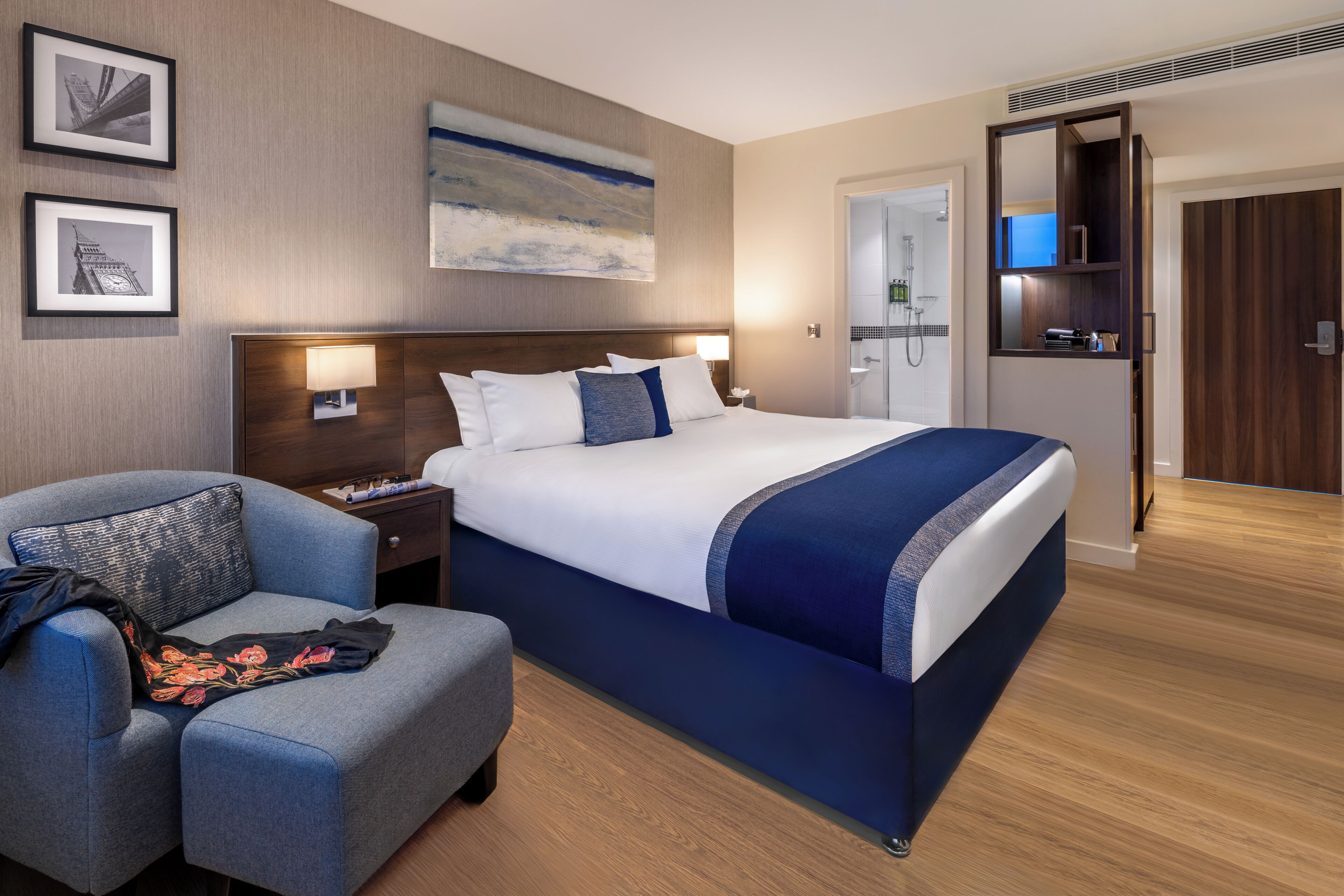 Habitación de hotel con una cama grande, un escritorio, una silla, un televisor y un baño visible a través de una puerta abierta.