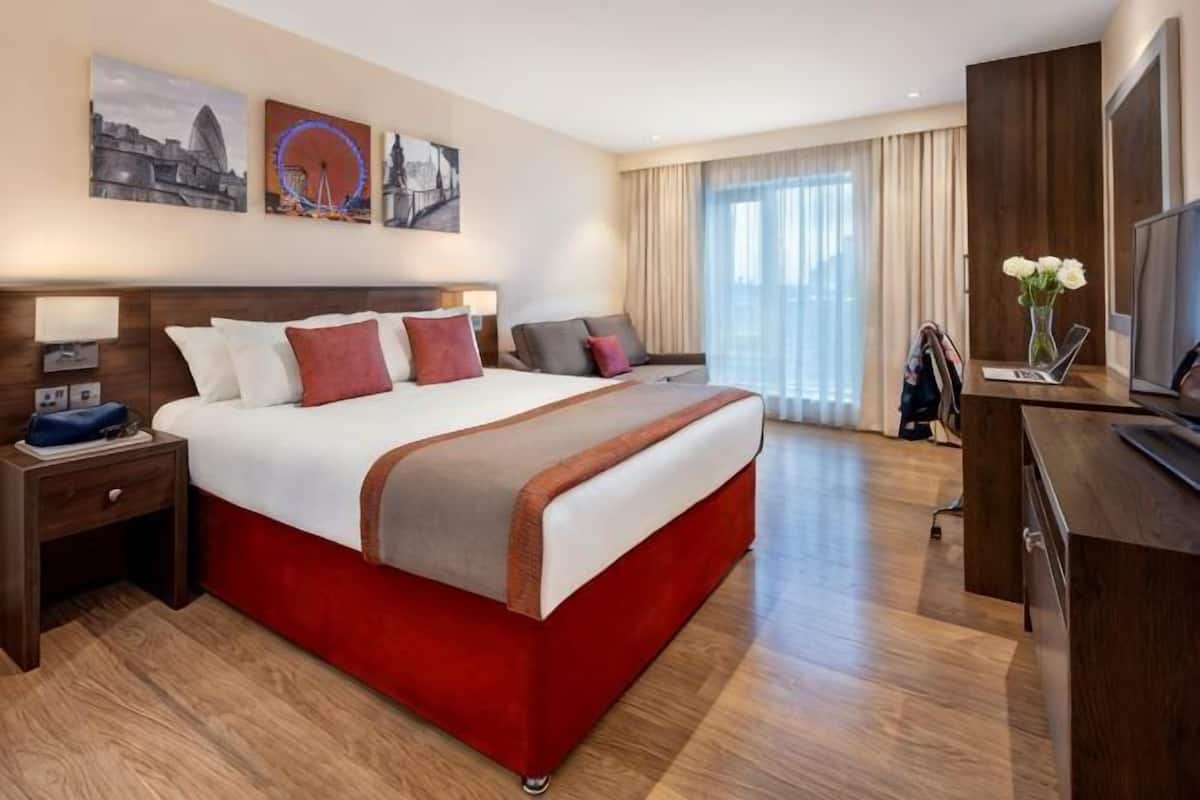 Une chambre d’hôtel avec un grand lit, un bureau, une télévision et une fenêtre avec des rideaux.