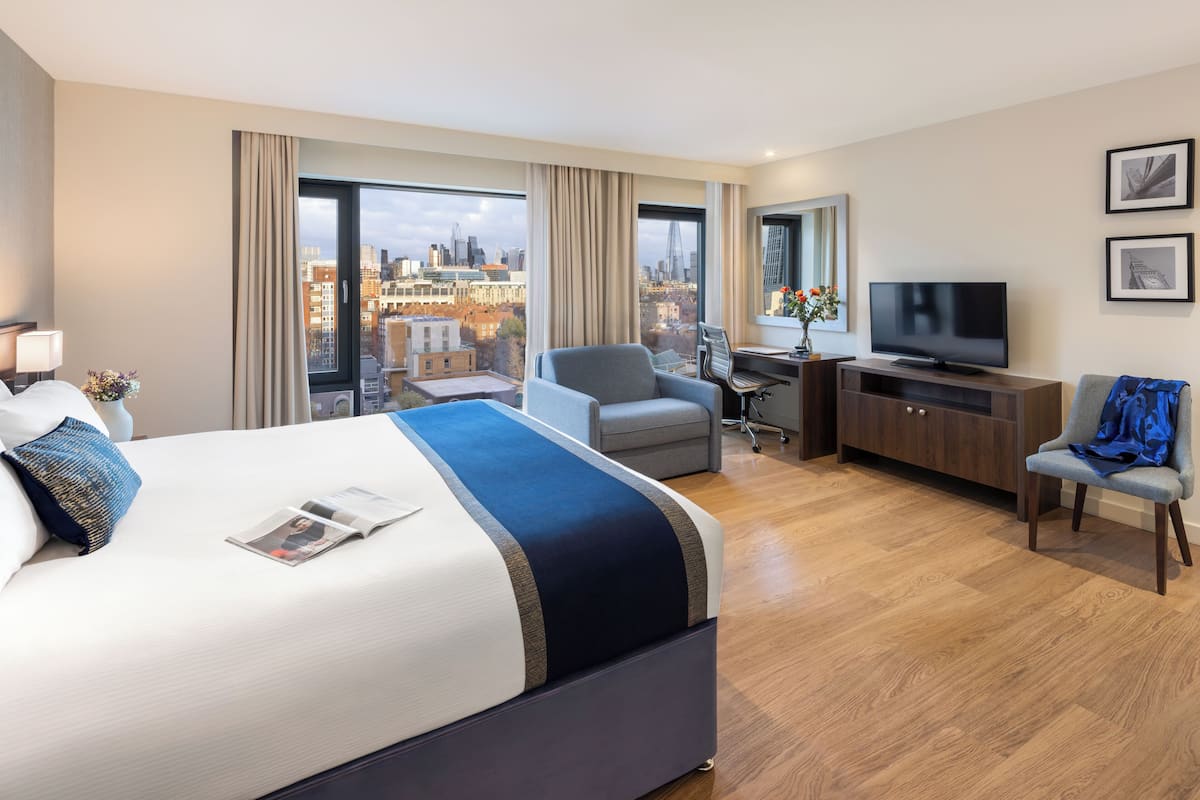 Une chambre d’hôtel moderne dotée d’un grand lit, d’un bureau, d’une télévision et offrant une vue sur le paysage urbain.