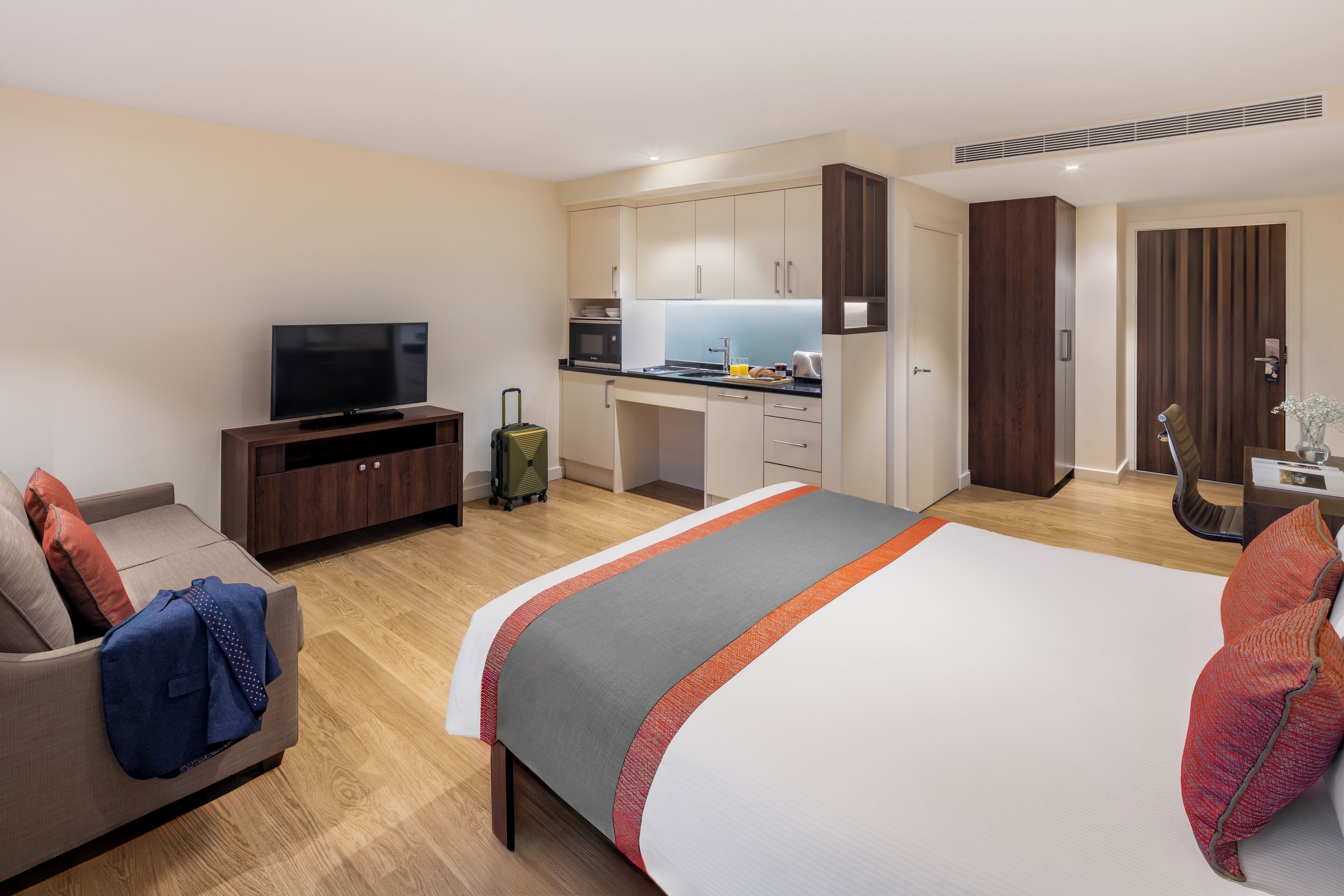 A hotel room with a bed, a TV, a kitchenette, and a sofa.