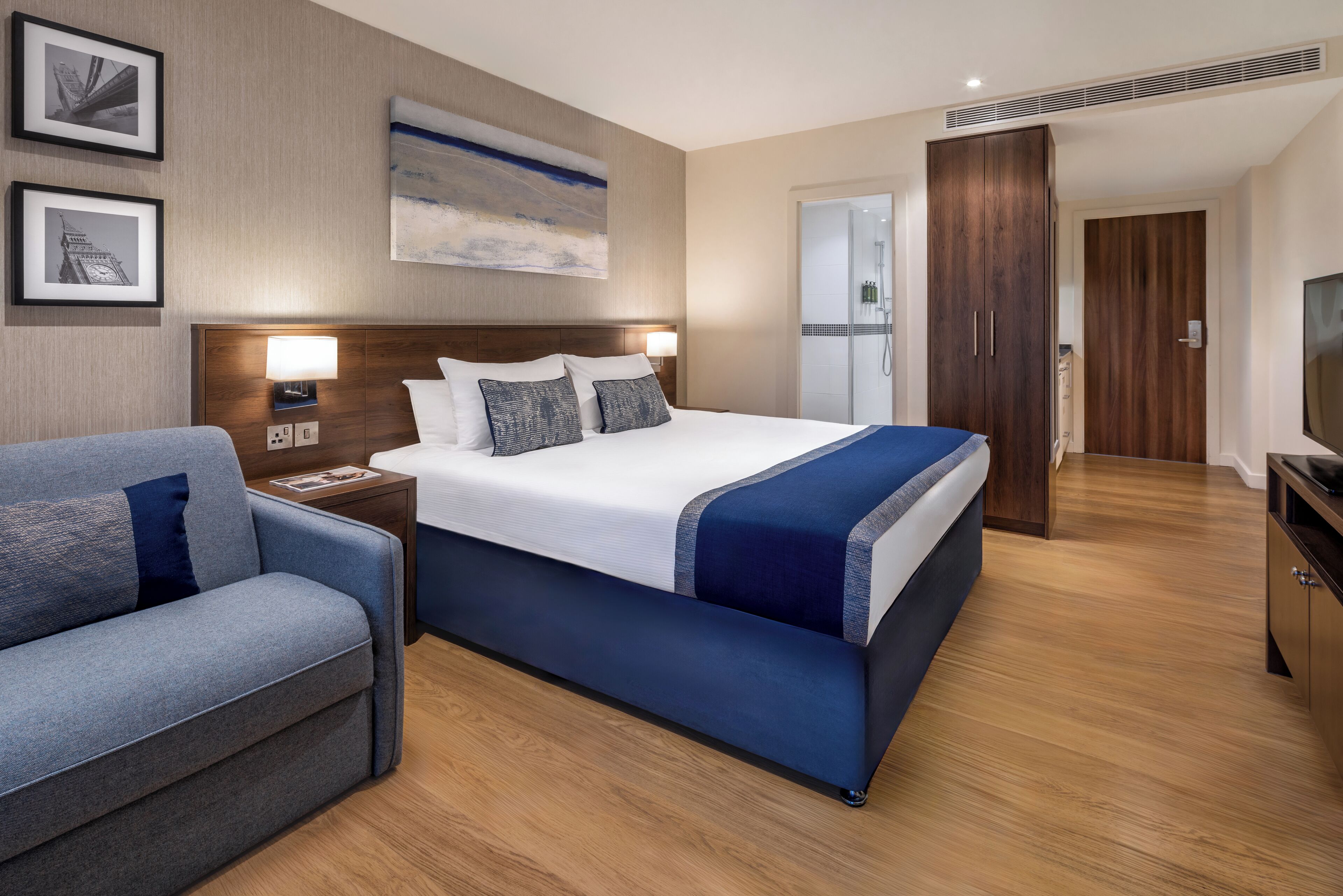 Ein Hotelzimmer mit einem großen Bett, einem Schlafsofa, einem Nachttisch mit Lampe, einem Fernseher und einem Kleiderschrank.