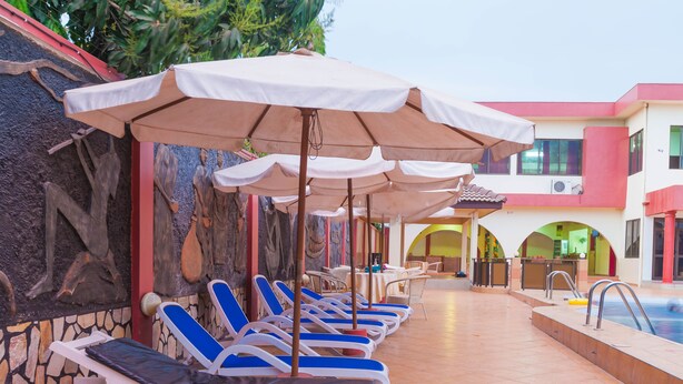 Un área junto a la piscina con sillones de descanso y sombrillas, una piscina y un edificio con arcos y una pared de piedra.
