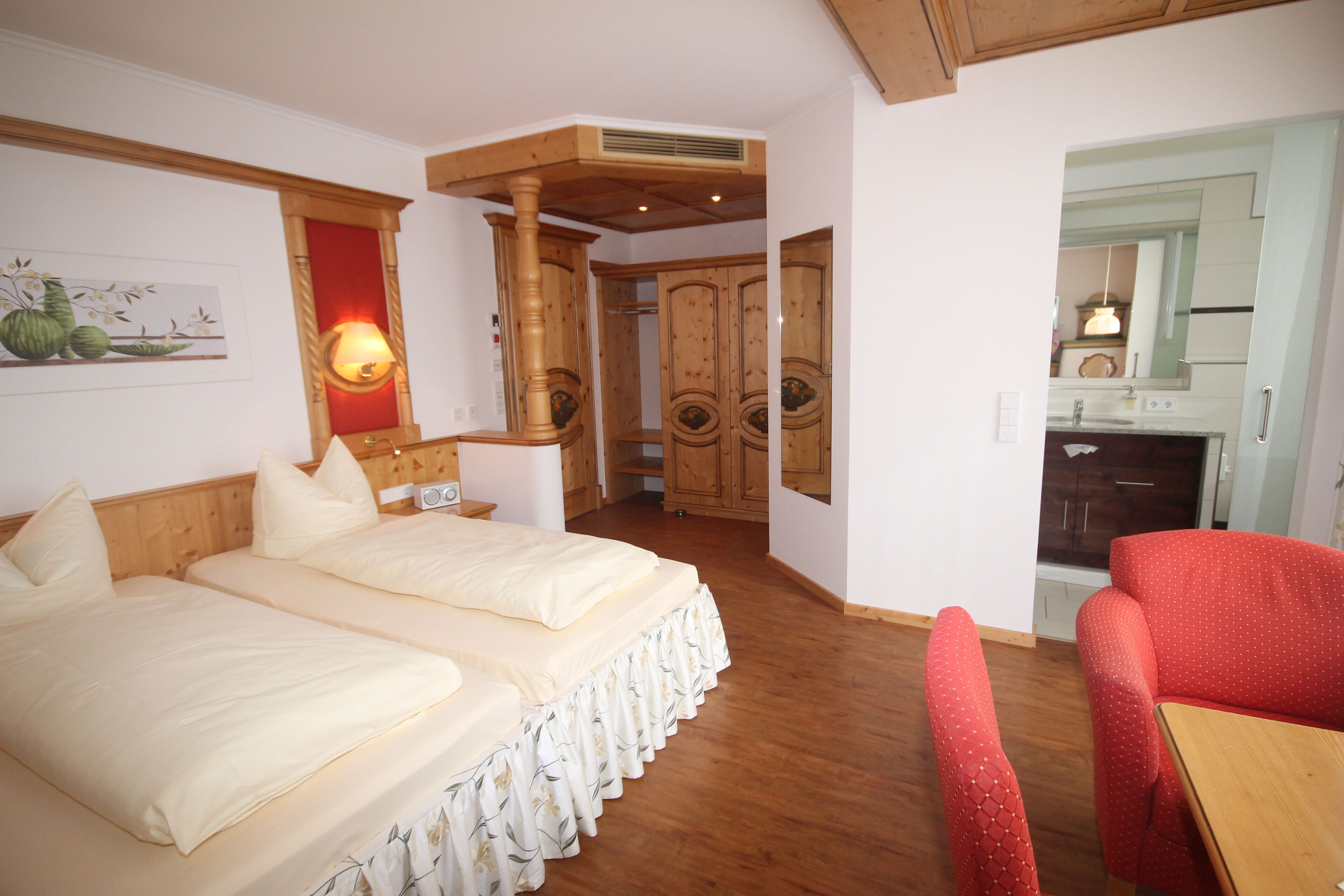Een hotelkamer met twee bedden, een houten plafond, een rode stoel en een kitchenette.
