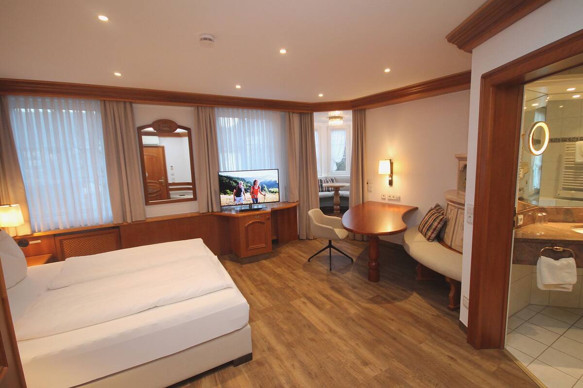 Habitación de hotel con cama, escritorio con computadora, silla, mesa redonda y baño con espejo y toallero.