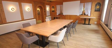 Un salón de conferencias con una larga mesa de madera, varias sillas y una pantalla de proyector.