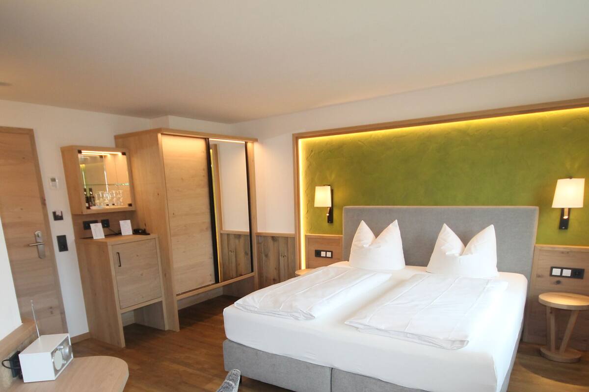 Habitación de hotel con cama, lámparas de noche, un espejo, armario y una mesita con lámpara.