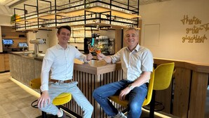 Dos hombres sentados en un bar de diseño moderno, con una barra de madera y una vitrina de vidrio.