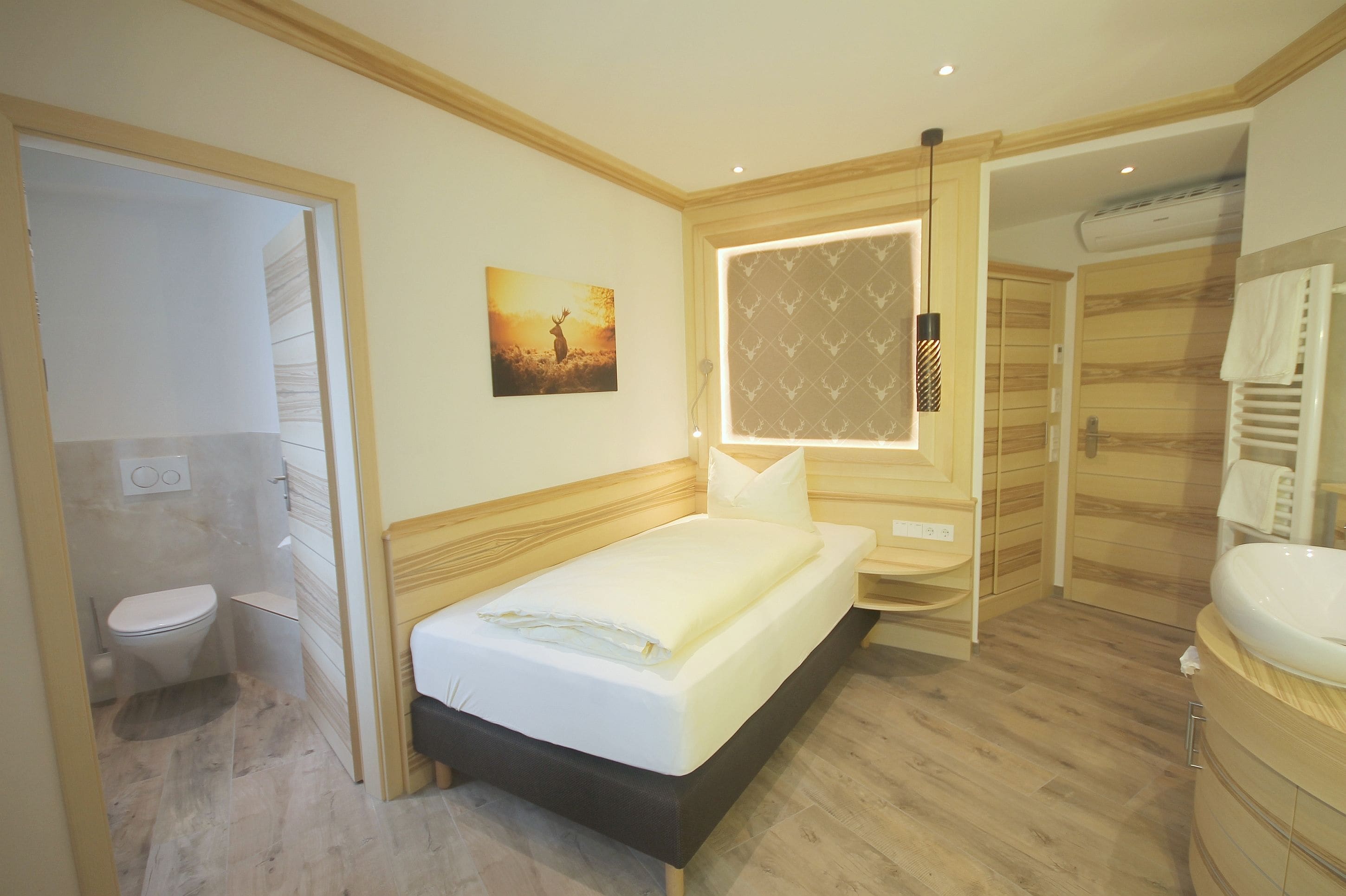 Habitación de hotel con cama, mesita de noche, espejo, ventana con vistas, baño con inodoro y lavabo, y suelo de madera.