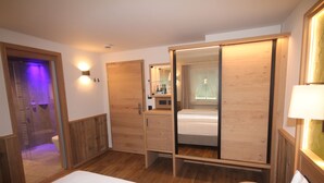 Una habitación de hotel con una cama grande, un armario de madera y una mesita de noche pequeña.