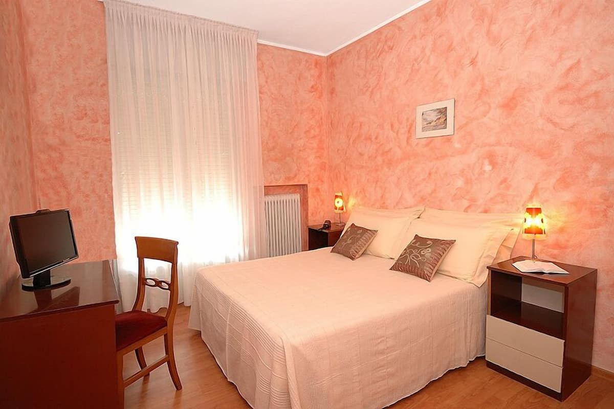Un dormitorio con cama, lámparas de noche, un escritorio con computadora y una silla.