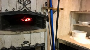 A traditional wood-fired oven with a fire burning inside, surrounded by a tiled wall with decorative metalwork. - Primavera Hotel (Mestre)