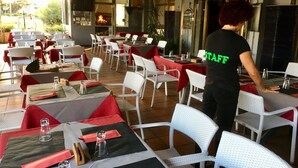 An outdoor restaurant with tables set for dining, a staff member in uniform, and a fire visible through the window. - Primavera Hotel (Mestre)