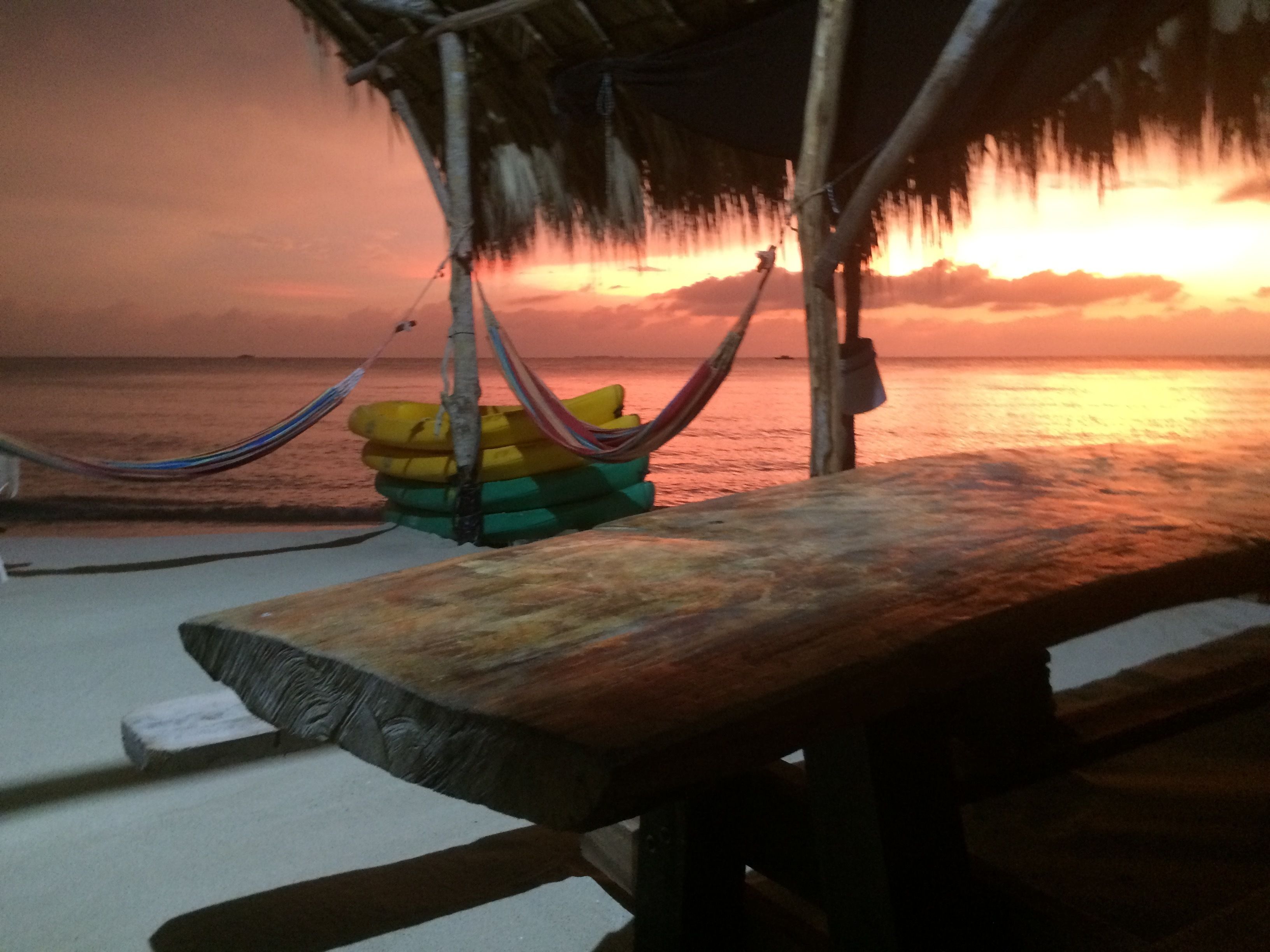 Un banco de madera en la playa con una hamaca y cojines de colores.