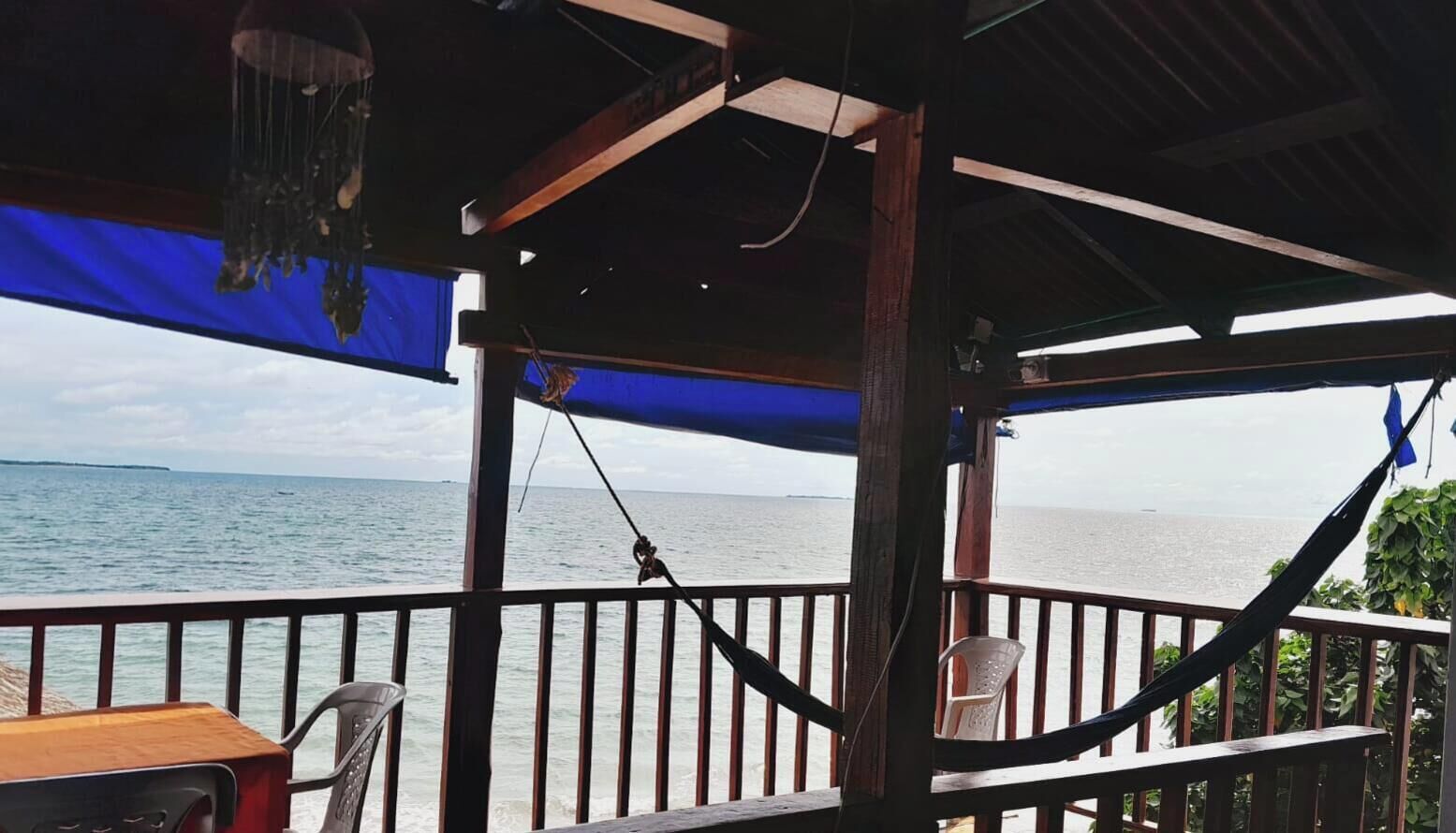 Una terraza de madera con vista al mar, una hamaca y una mesa con una silla.
