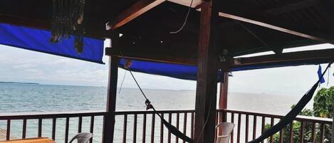 Una terraza de madera con vista al mar, una hamaca y una mesa con una silla.