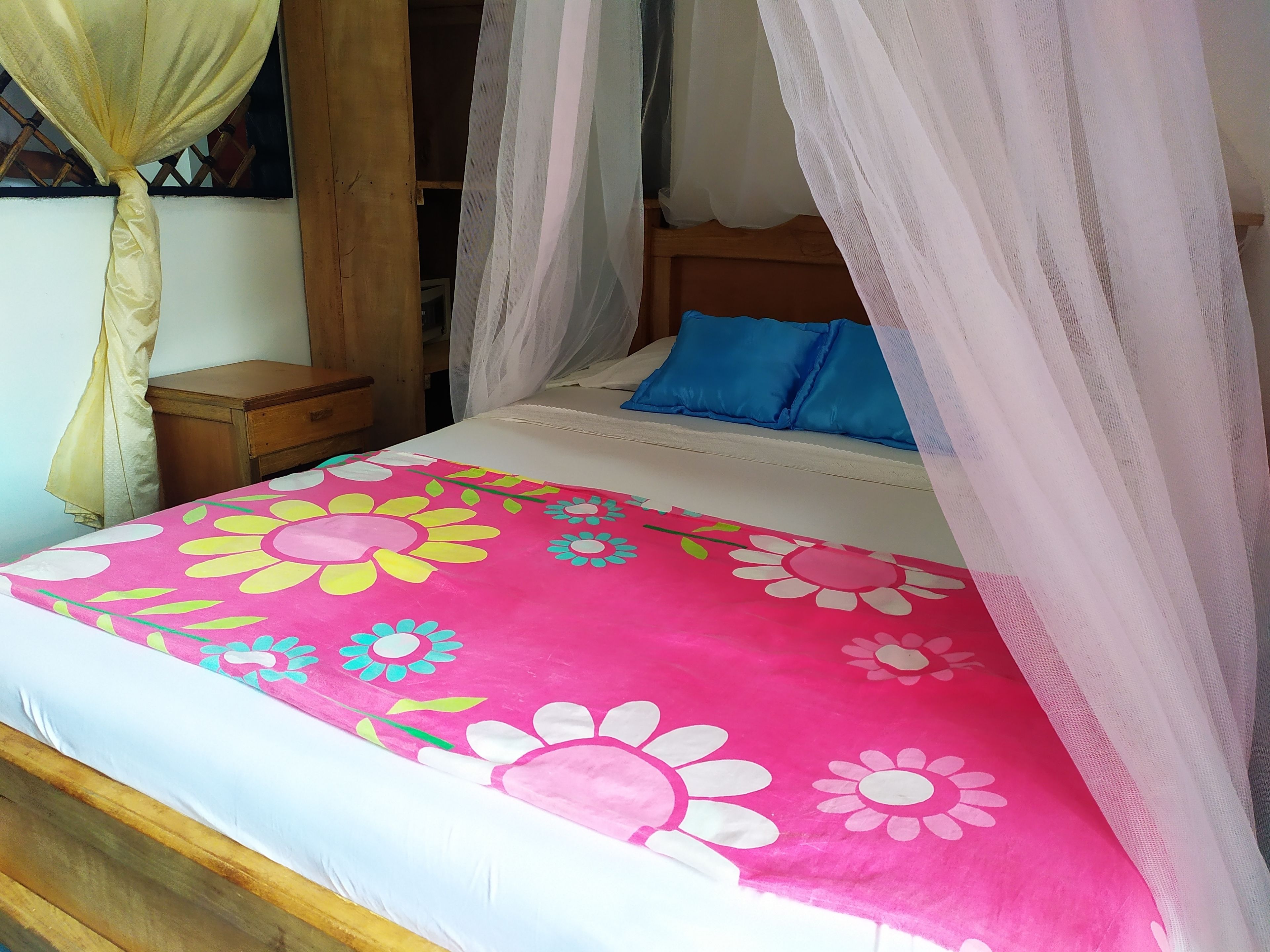 A bed with a floral bedspread, a wooden nightstand, a wooden headboard, and a canopy.