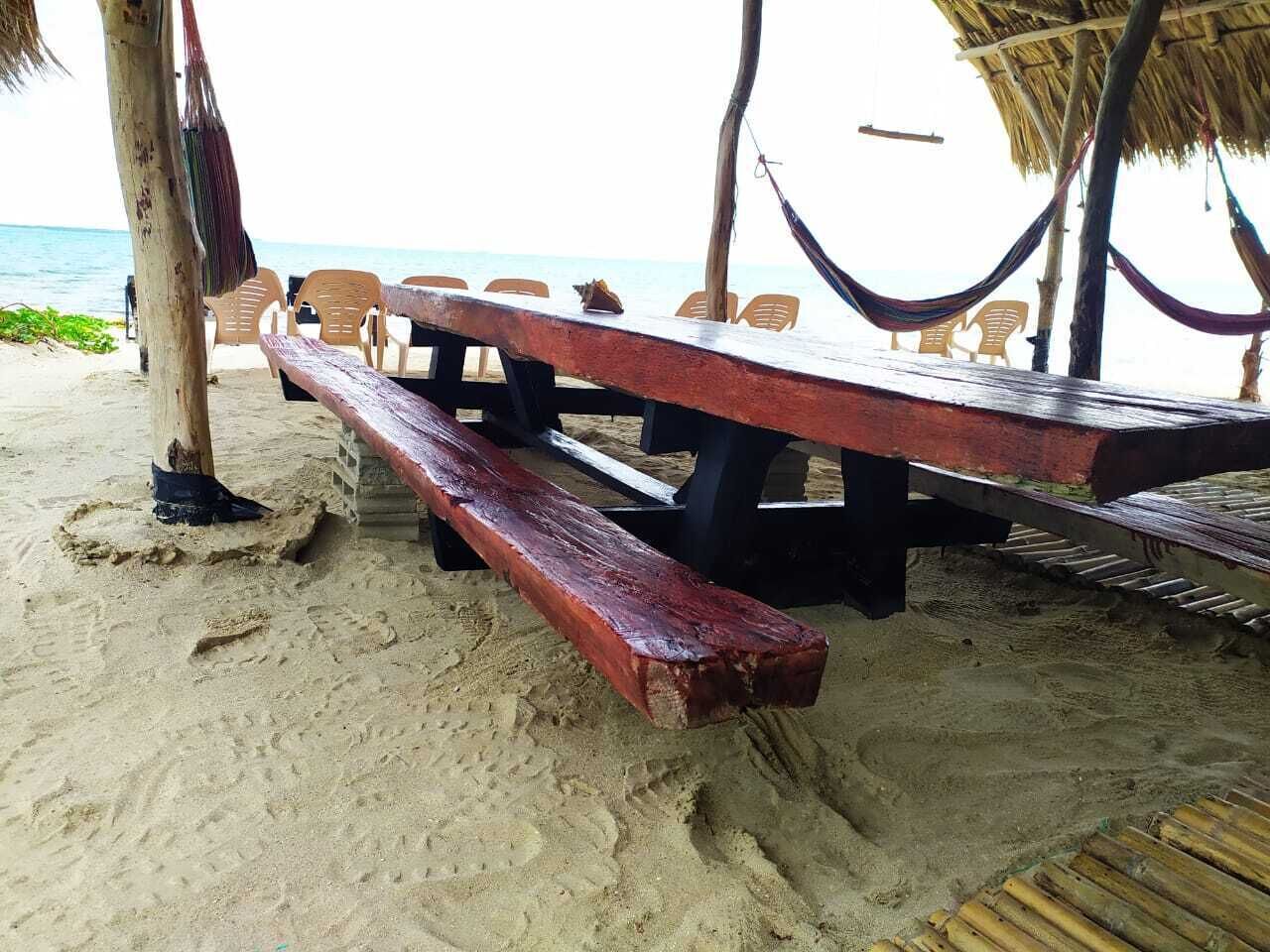 A beachside wooden bench area with a thatched roof, surrounded by plastic chairs.