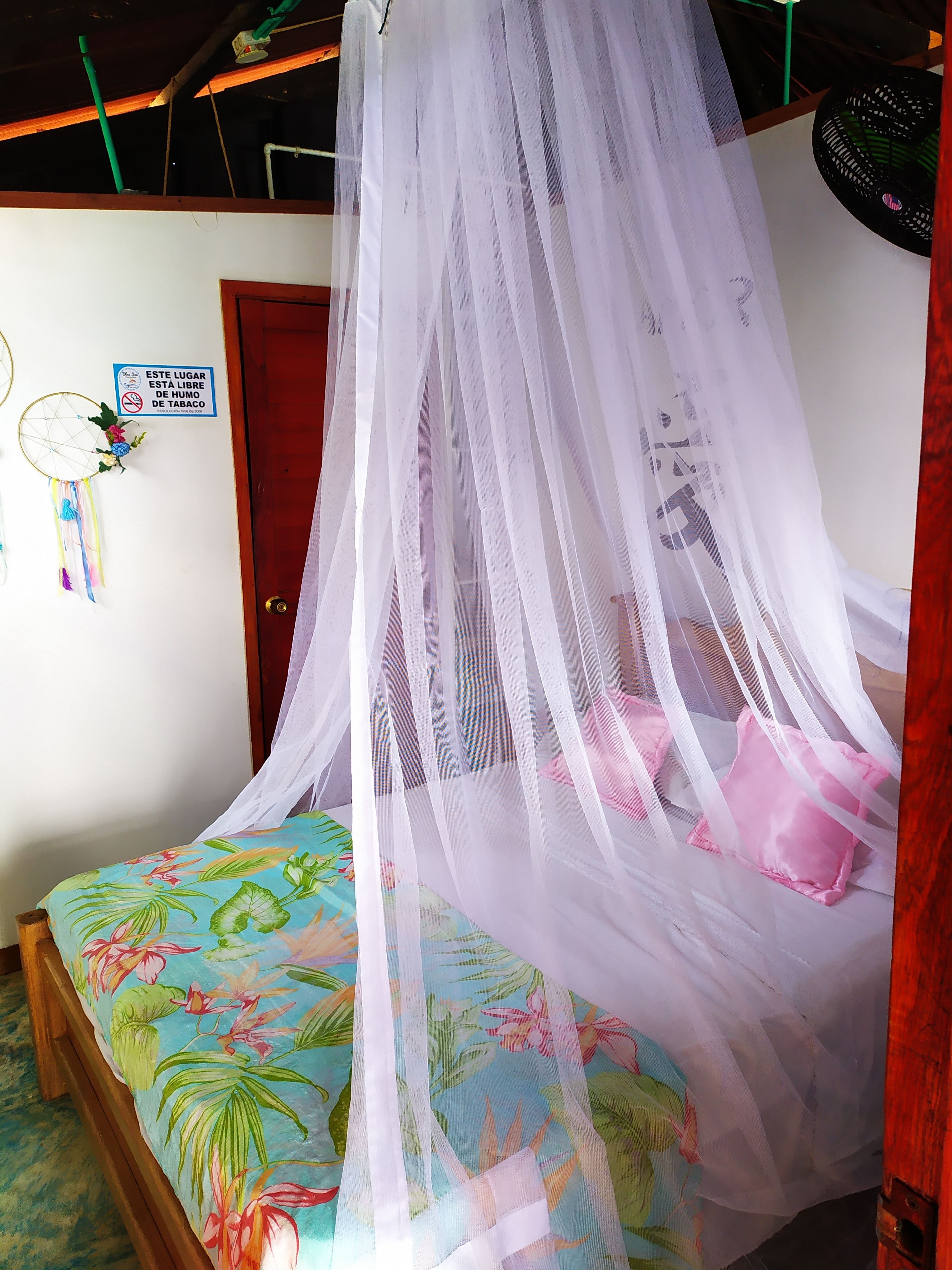 A bed with a floral bedspread, a white mosquito net, and a sign prohibiting smoking.