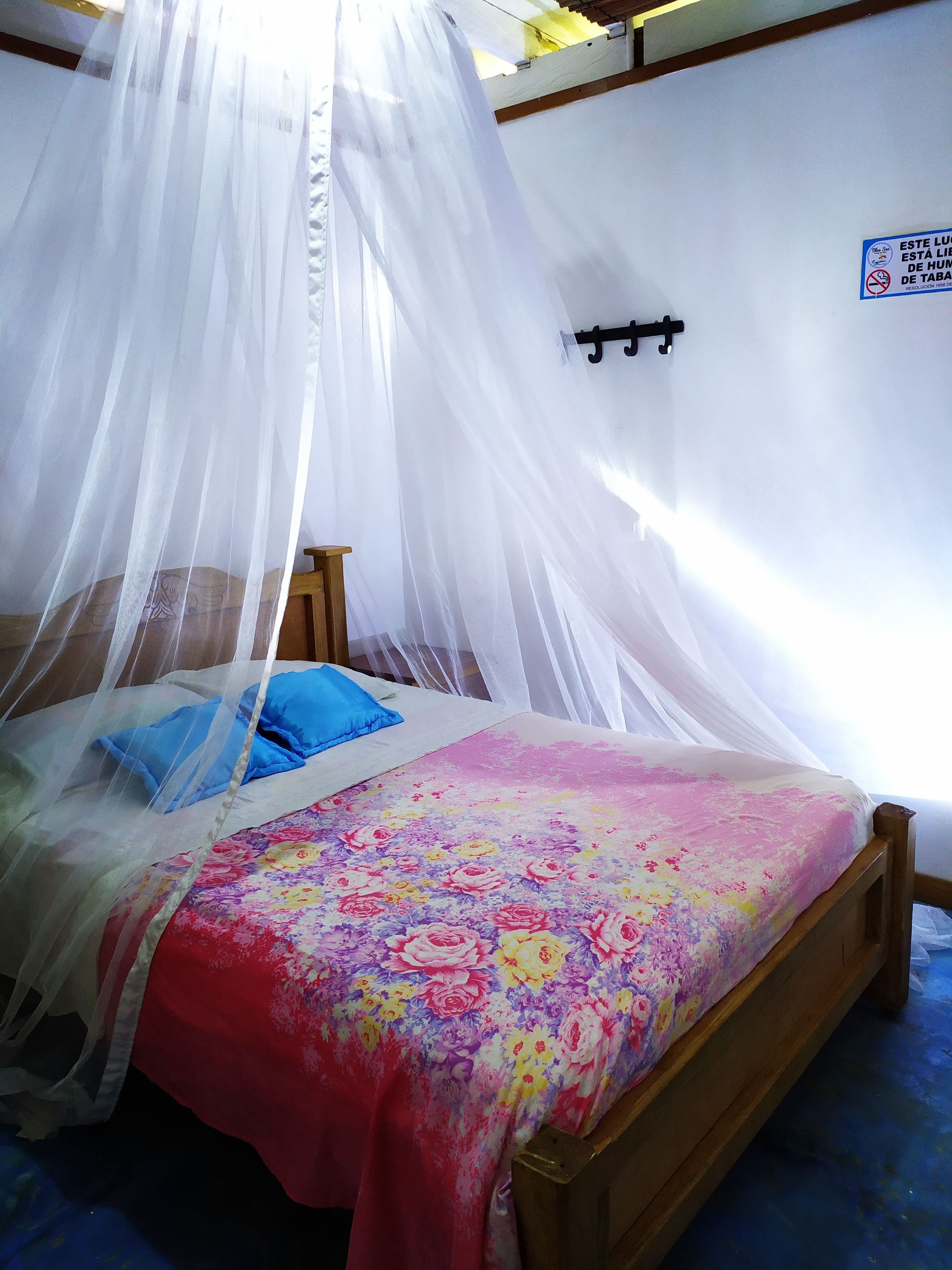 Ein Bett mit Blumenmuster auf der Tagesdecke, einem blauen Kopfkissen und einem weißen Moskitonetz.
