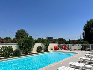 A swimming pool with lounge chairs and a fenced area with red chairs. - Brit Hotel Salon de Provence (Salon-de-Provence)