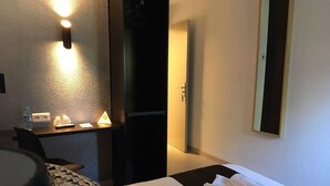 Une chambre d’hôtel avec un lit, un bureau avec une lampe, un miroir et une porte de salle de bain.