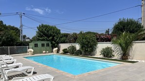 Une piscine rectangulaire entourée de chaises longues blanches.