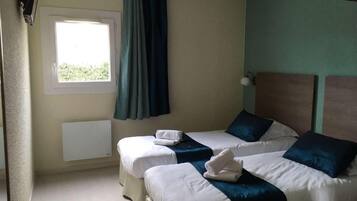 A hotel room with two beds, a window with curtains, a radiator, and a wall-mounted lamp.