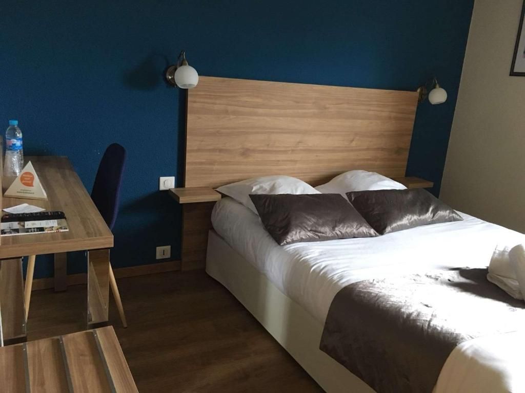 A hotel room with a wooden headboard, a bed with white and dark pillows, a bedside table with a water bottle and a book, and a lamp on the wall.