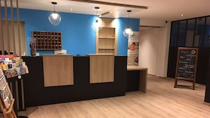 Un hall d’accueil d’hôtel avec un mur bleu, un comptoir d’accueil en bois et un tableau noir où sont écrits des messages de bienvenue.