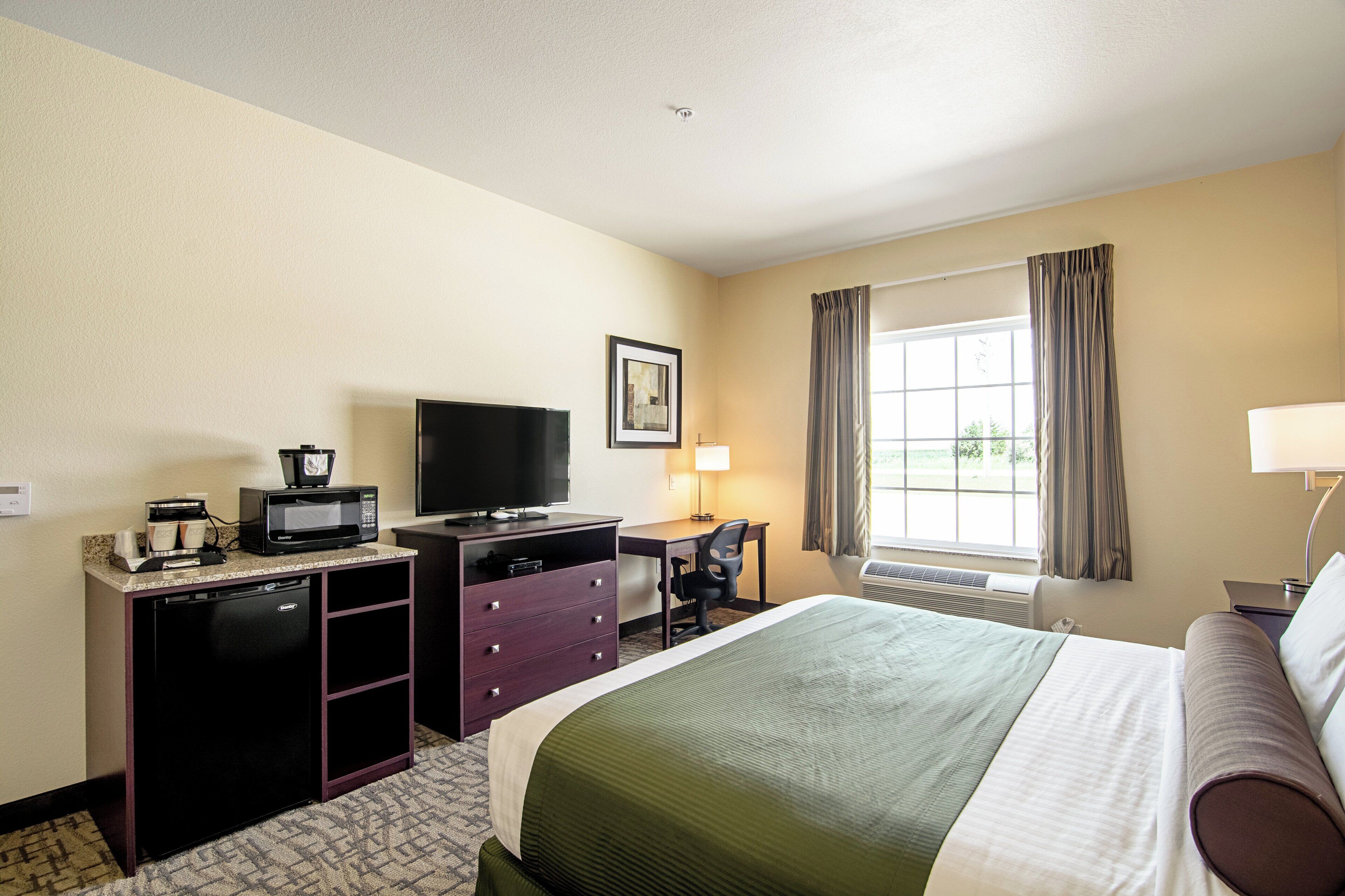 A hotel room with a bed, a desk, a television, a microwave, and a window with curtains.