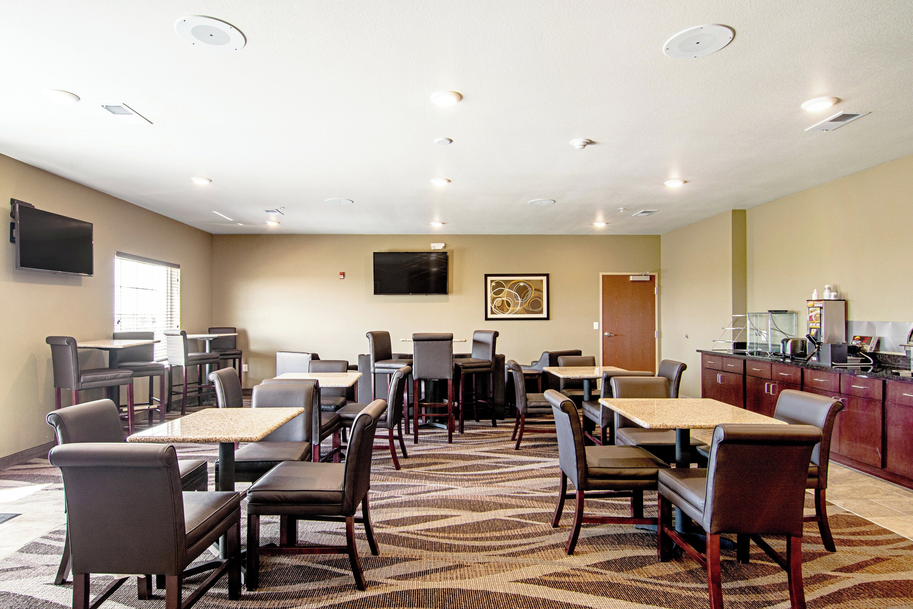 Een restaurantgedeelte in een hotel met meerdere tafels en stoelen, een flatscreen televisie aan de muur en een keuken met apparatuur.