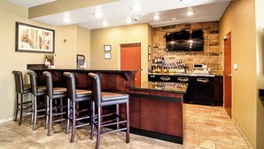 A bar area with a stone wall, a flat-screen TV, and a bar counter. - Cobblestone Hotel & Suites - Paxton (Paxton)