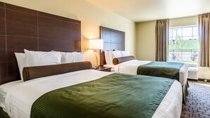 A hotel room with two beds, a large window with curtains, a lamp, and a view of the outdoors. - Cobblestone Hotel & Suites - Paxton (Paxton)
