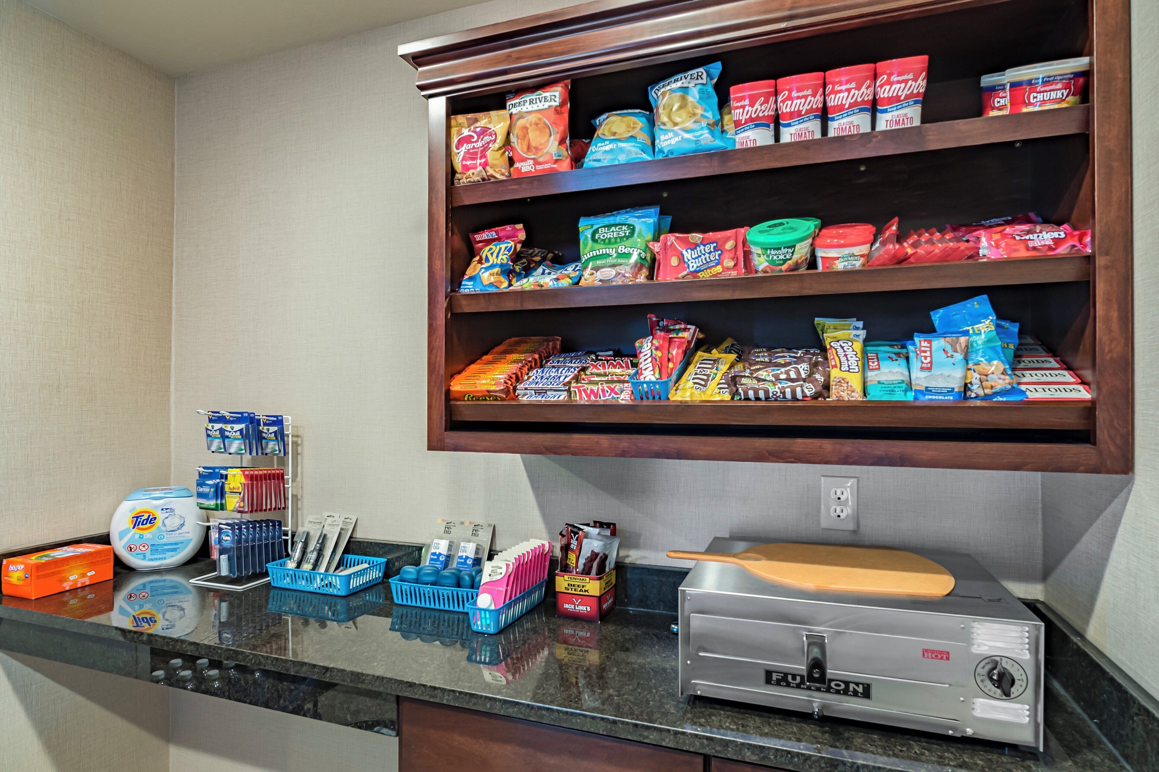 A kitchen area with a shelf stocked with snacks and a countertop with cleaning supplies and a coffee machine.