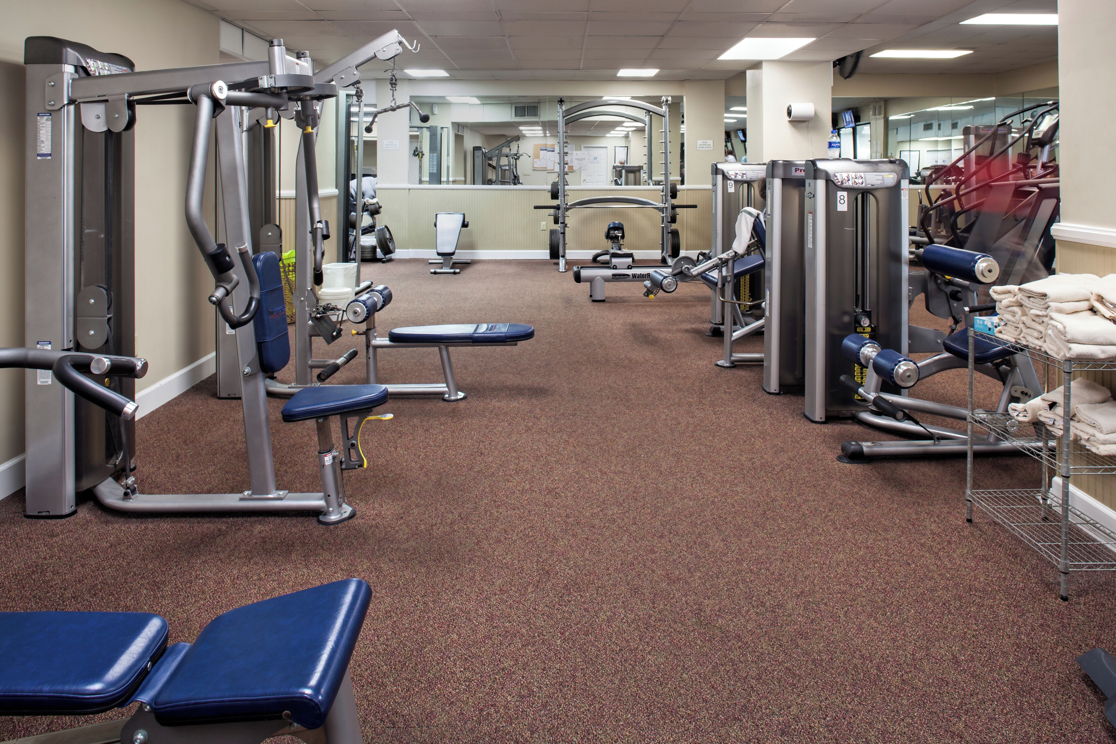 Ein Fitnessstudio mit verschiedenen Trainingsgeräten, Bänken und einer Spiegelwand.