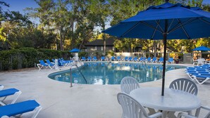 A poolside area with blue lounge chairs, a pool, and a table with chairs.
