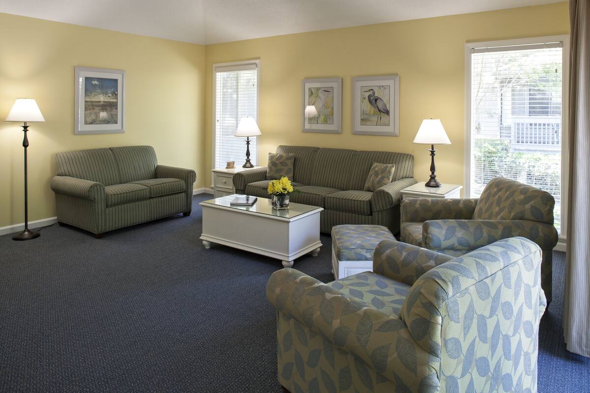 A living room with a striped sofa, a patterned armchair, a white coffee table with flowers, and two lamps.