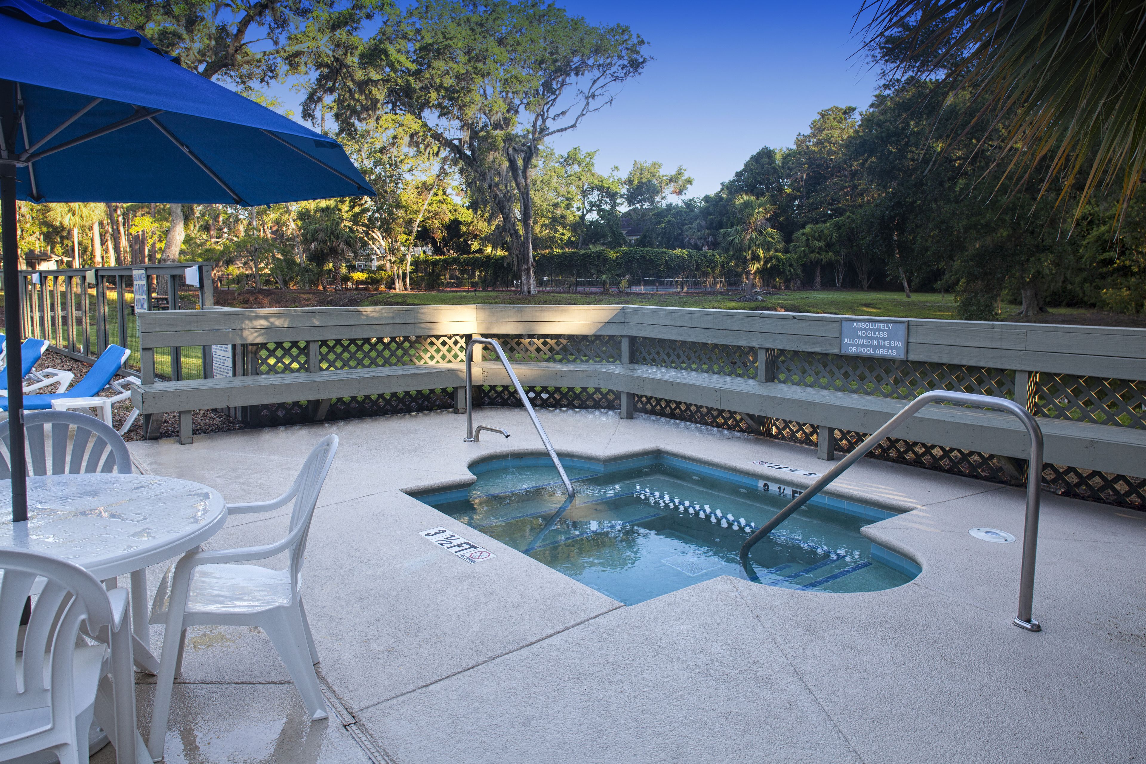 An outdoor swimming pool with a metal ladder, surrounded by a fence and a bench.