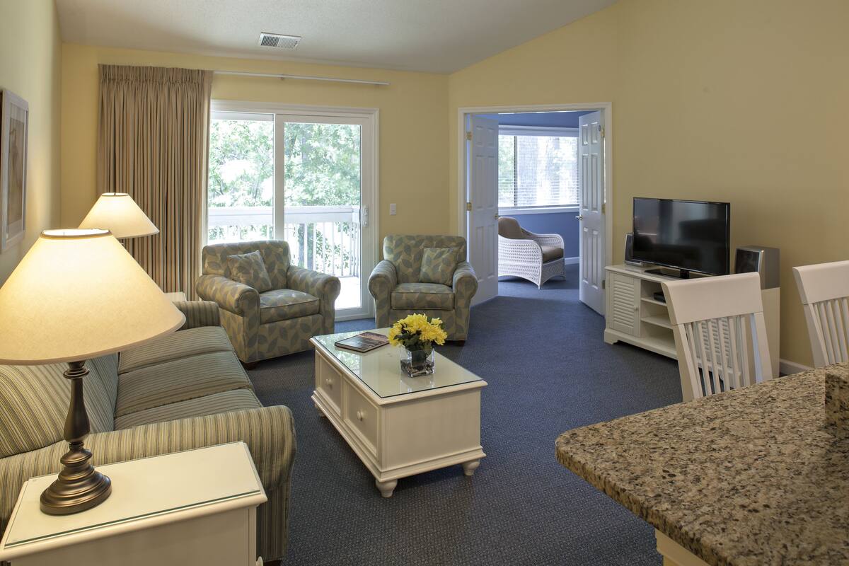 A hotel room with a sofa, armchair, and a television on a stand.