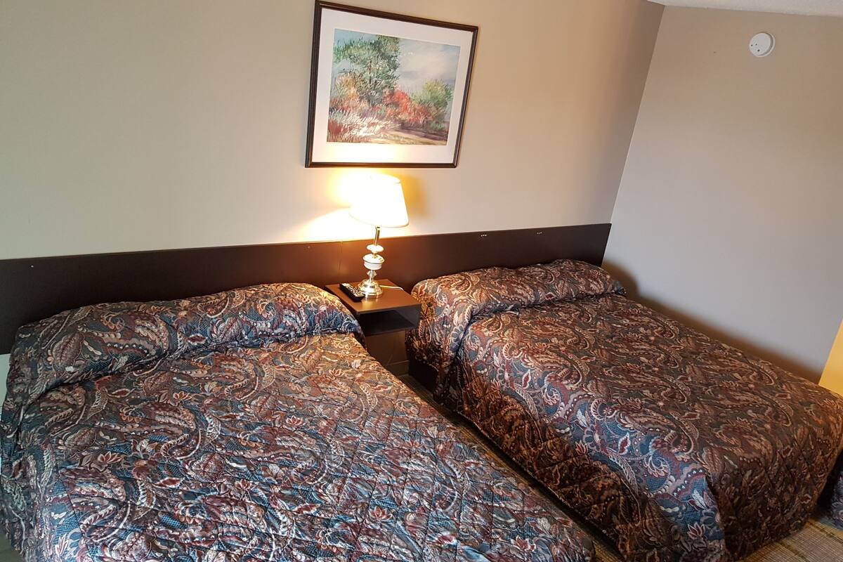 A hotel room with two beds, a nightstand with a lamp, and a framed picture on the wall.