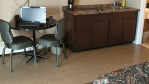 Una camera d'albergo compatta con angolo cottura, una scrivania con un portatile, due poltrone con motivi decorativi, un letto con copriletto a fantasia e una televisione a parete.